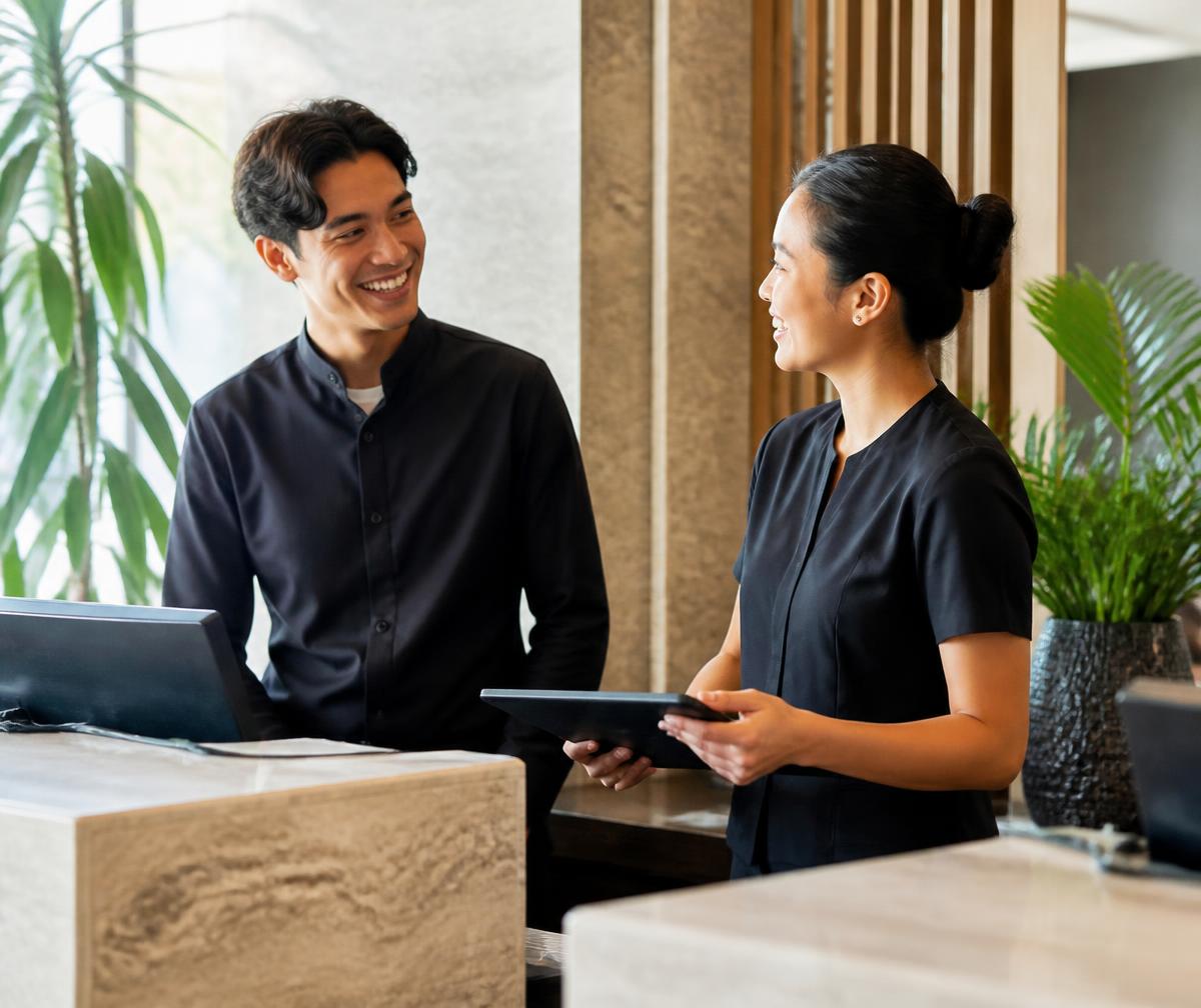 Two hospitality team members talking warmly behind a bright hotel reception.